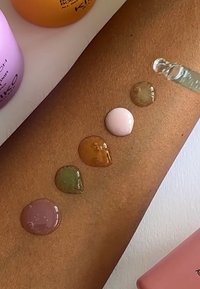 Prodotti di bellezza KIKO mostrati con gocce liquide su un braccio marrone: rosa chiaro, verde, marrone e rosa scuro, che evidenziano diverse texture.