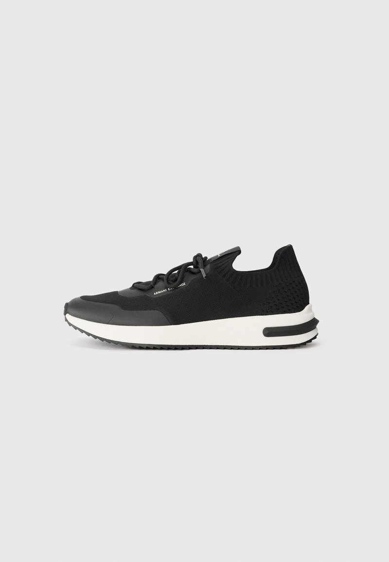 Pantofii sport negri au un superior din material tricotat, cu vârf rotunjit și o talpă albă contrastantă, dotată cu un grip texturat. Șireturile sunt integrate în design.