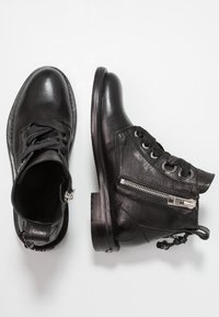 Botas de piel negra hasta el tobillo con un acabado texturizado, punta redonda, parte delantera con cordones y cremallera lateral con acentos metálicos. Suela plana.