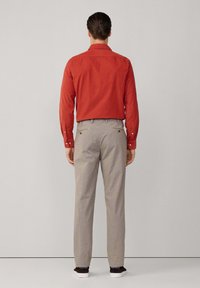 Camisa roja de manga larga con cuello, combinada con pantalones de cuadros en gris claro. Los pantalones tienen un corte relajado y bolsillos traseros.