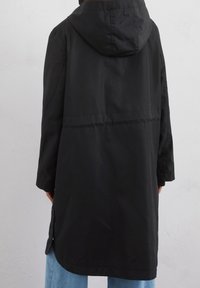 Svart huvjacka i parka-stil med en slät textur, knälång design, sidoventiler och långa ärmar. Minimalistisk stil utan synlig hårdvara.