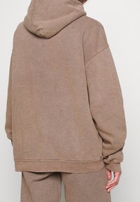 Brązowa, oversize bluza z kapturem, wykonana z miękkiego materiału. Charakteryzuje się luźnym krojem, ściągaczami na rękawach oraz prostym dołem. Minimalistyczny design.