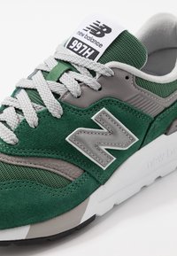 Zeleno-šedé tenisky New Balance 997H vyrobené z usně a síťoviny, se zvýrazněným šedým logem "N", texturovanými tkaničkami a bílou podrážkou.