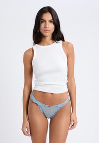 Top sin mangas blanco con costuras acanaladas, combinado con un delicado tanga azul de encaje, con bordes festoneados y un pequeño acento rosa en el centro.