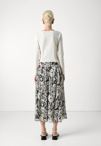 Hvit langermet topp og svart blomstrete maxiskjørt med hvit broderi. Har en utsvingt design og svarte sandaler med ankelrem.