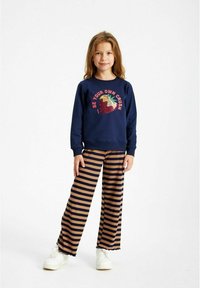 Felpa navy con grafica di fragola e testo, abbinata a pantaloni a gamba larga a righe beige e navy e sneakers bianche.