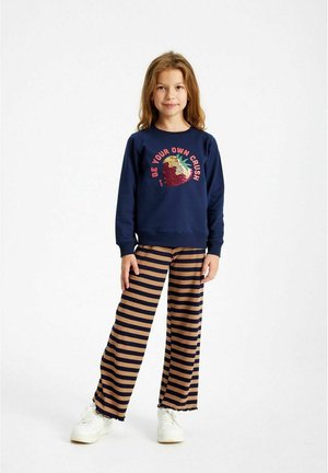 Felpa navy con grafica di fragola e testo, abbinata a pantaloni a gamba larga a righe beige e navy e sneakers bianche.