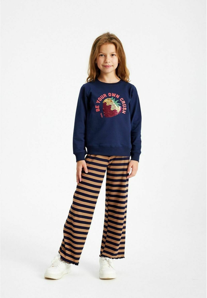 Felpa navy con grafica di fragola e testo, abbinata a pantaloni a gamba larga a righe beige e navy e sneakers bianche.