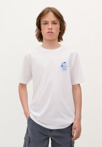 Weiße Baumwoll-T-Shirt mit kurzen Ärmeln, ausgestattet mit einem blauen Eiscreme-Grafikdesign auf der linken Brusttasche. Schlichte Textur, reguläre Passform.