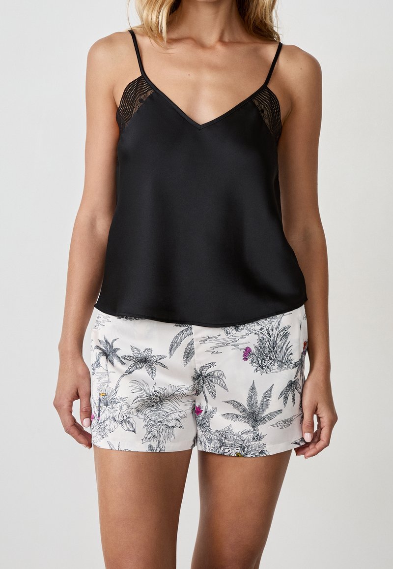 Camisole en satin noir à fines bretelles, avec des accents en dentelle ; assortie à des shorts blancs ornés d'un imprimé botanique noir et de fleurs colorées.