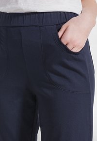 Námořnicky modré volné kalhoty s elastickým pasem, vybavené bočními kapsami a měkkou, texturovanou látkou. Čisté švy.