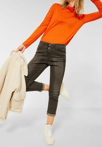 Oranžový dlouhý rukáv, černé a šedé kostkované kalhoty se dvěma knoflíky, zkrácená délka, strukturovaná tkanina, doplněné bílými teniskami a béžovým kabátem.