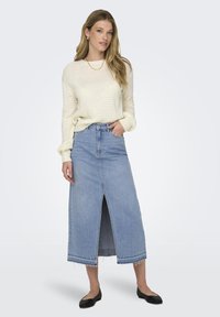 Pull en tricot de couleur crème clair à manches longues associé à une longue jupe en denim bleu avec une fente avant et un ourlet effiloché, complété par des ballerines noires.