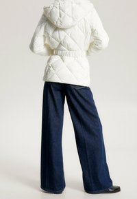 Chaqueta de plumón acolchada blanca con capucha y cintura ceñida, combinada con pantalones vaqueros oscuros de corte holgado, vista desde atrás.