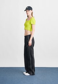 Pulover scurt de culoare verde neon, textură moale, decolteu pătrat; pantaloni de sport negri cu dungi albe pe lateral, talie elastică; pantofi albi slip-on.