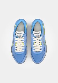 Μπλέ υφασμάτινα αθλητικά παπούτσια με λευκά κορδόνια, γκρίζες σόλες και νεον κίτρινες λεπτομέρειες. Διαθέτουν μαλακή γλωττίδα και λεπτομέρεια με λογότυπο στο πλάι.