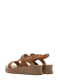 Sandalias de cuero trenzado marrón con correas de tobillo ajustables y suela de plataforma texturizada, con estrías horizontales y un acabado suave.