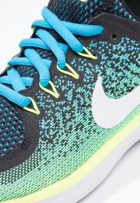 Černá a tyrkysová sportovní bota s síťovaným svrškem, jasně modrými tkaničkami, žlutými akcenty a výrazným bílým logem swoosh na boku.