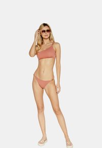 Costume da bagno a due pezzi color terracotta. Top a spalla unica in tessuto morbido e design minimalista, abbinato a classiche mutande bikini.
