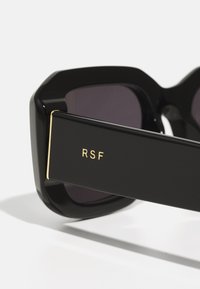 Black sunglasses with an octagonal shape, dark lenses, and a bold, flat arms featuring a gold "RSF" logo detail.