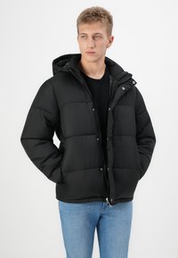 Chaqueta de abrigo negra con capucha, con un diseño acolchado, cierre frontal de cremallera y botones. El material parece suave y ligeramente brillante.