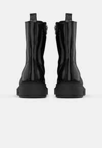 Botine negre din piele lacuită cu talpă groasă, închidere cu fermoar pe lateral și mânere pe spate. Textură netedă și design elegant.