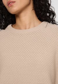 Gestrickter Pullover in hellbeige, mit einem strukturierten Muster, weitem Rundhalsausschnitt und gerippten Bündchen. Weich gewebter Stoff mit einem gemütlichen Erscheinungsbild.