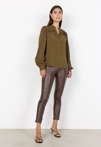 Olive green blouse with button front and pleated details, paired with brown slim-fit leather pants and black strappy heels.