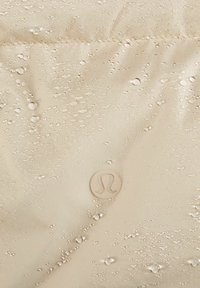 Tissu imperméable beige avec des gouttes d'eau et un logo Lululemon circulaire embossé au centre.