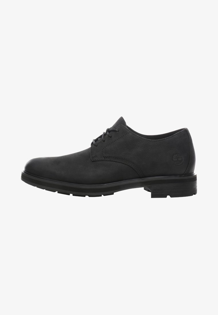 Chaussure habillée noire en cuir à lacets, talon bas et bout rond, vue latérale montrant le logo Timberland embossé sur la zone du talon.