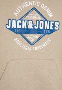 Felpa beige con cappuccio, caratterizzata da una grande grafica blu e bianca con il testo "JACK & JONES", un design triangolare e una tasca frontale.