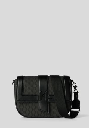 Czarna torebka na ramię z fakturowanym wzorem, skórzanym zapięciem i szerokim regulowanym paskiem na ramię z materiału na tle jednolitym.