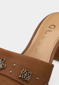 Καφέ σουέντ μπαλαρίνα με μεταλλικά διακοσμητικά σε σχήμα χελώνας και καβουριού και μπεζ εσωτερική σόλα με την επωνυμία «GUESS».