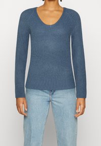 Långärmad, djupblå stickad tröja med ribbat mönster och rundad halsringning, ihop med ljusblå jeans.