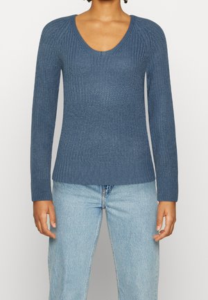 Pull en tricot bleu profond à manches longues avec texture côtelée et encolure dégagée, associé à un jean bleu clair.
