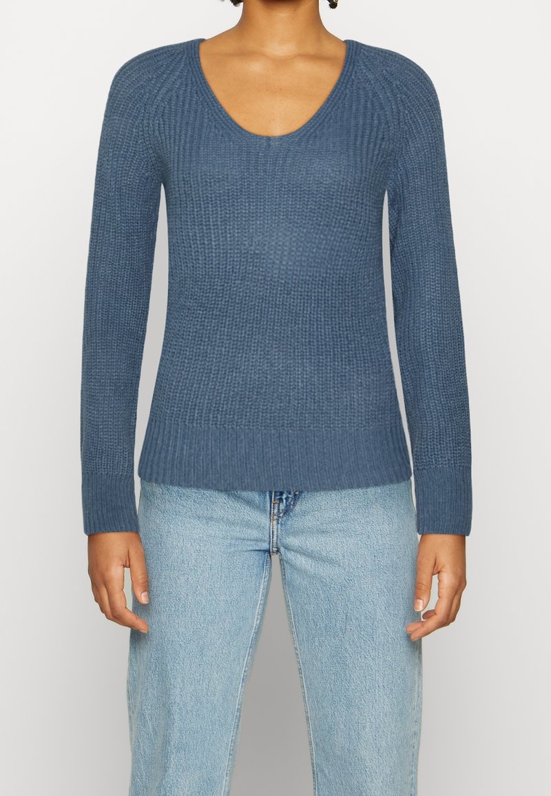 Långärmad, djupblå stickad tröja med ribbat mönster och rundad halsringning, ihop med ljusblå jeans.