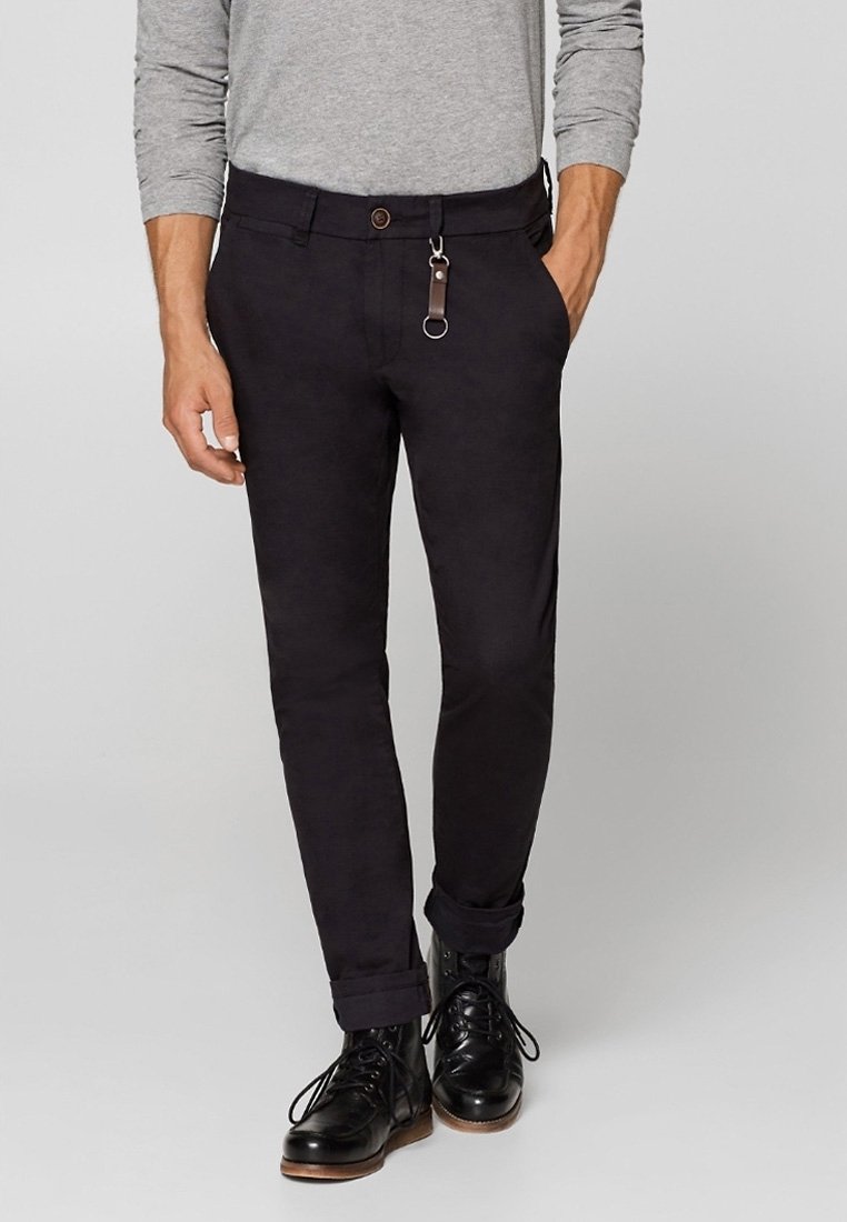 Pantaloni neri dal taglio slim, con un bottone marrone, passanti per cintura e un accento in pelle. Il tessuto appare liscio con un leggero lucido.
