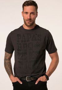 Schwarzes Baumwoll-T-Shirt mit einem markanten, abgenutzten Schriftzug, der "PAPA'S BBQ THE BEST IN TOWN" lautet. Kurzärmlig und mit Rundhalsausschnitt.