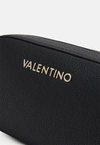 Geantă din piele texturată neagră cu logo-ul auriu "VALENTINO". Prezintă o formă rotundă și un model subtil de granulație pe suprafață.
