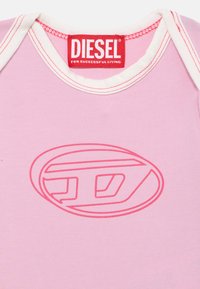 Ružová polokošeľa s krátkym rukávom a bielym golierom, na prednej strane s prominentným ružovým logom Diesel. Vyrobená z jemného bavlneného jersey materiálu.