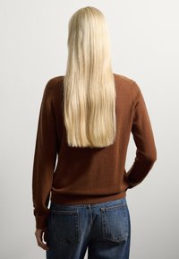 Brauner Strickpullover mit langen Ärmeln, gerippten Bündchen und Rundhalsausschnitt, kombiniert mit blauen High-Waist-Jeans. Glatte Textur, schlichtes Design.