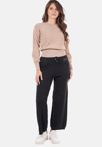 Pantaloni neri a gamba larga con vita elastica e coulisse, abbinati a un maglione leggero beige texture. Il modello indossa sneakers bianche.