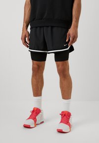 Black athletic shorts layered over black compression shorts, finished with a white trim; worn with white socks and pink-and-white sneakers.