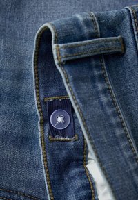Tamno plavi jeans tkanina s vidljivim šavovima, s prozirnim plastičnim dugmetom i s rebrastom tkaninom na pojasu.