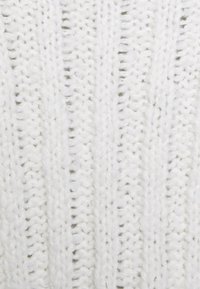 Bílá pletená látka s vertikálním žebrovaným vzorem. Příze je tlustá a měkká, což vytváří útulný a teplý vzhled.