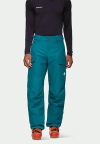 Zöldeskék hóruha két oldalsó zsebbel, harang szabású dizájnnal és logóval a jobb lábon. Fekete hosszúujjú toppal és narancssárga csizmával párosítva.