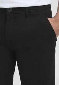 Schwarze Hosen aus weichem Stoff, mit Knopfverschluss, vorderen Taschen, slim fit und subtilen Nähten.