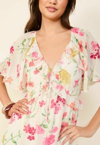 Robe fleurie en tissu léger et transparent avec un décolleté en V, des manches volantées et une taille à cordon, arborant des motifs roses, jaunes et verts.