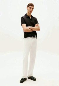 Camisa polo preta, calças brancas e mocassins pretos. O conjunto apresenta um ajuste sob medida, cores contrastantes e um design minimalista.