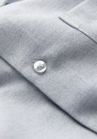 Gros plan sur un tissu gris clair avec un bouton cousu et un bord plié, montrant la texture et le détail du textile.